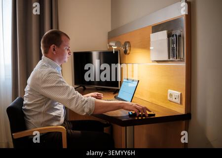 Businessman using laptop and smartphone at a desk in a hotel room Stock Photo