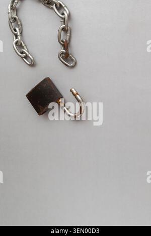A close-up of an open, rusty vintage padlock completely separated from a metal chain on a gray background. Stock Photo