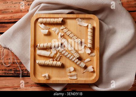 Crispy wafer rolls filled with chocolate cream served on a rustic square bamboo plate over a textured cloth. Food photography with space for text. Stock Photo