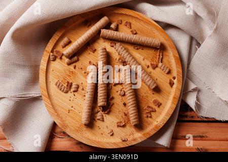 Crispy wafer rolls filled with chocolate cream served on a rustic bamboo plate over a textured cloth. Top view Stock Photo