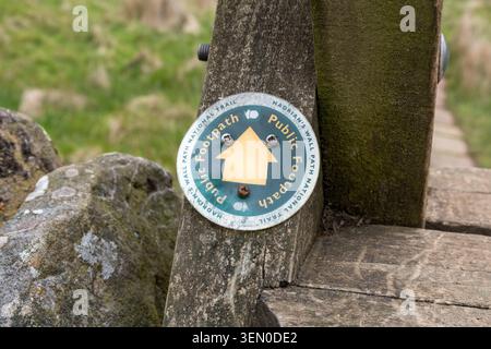 A public footpath sign on a wooden stile crossing a stone wall along the historic Hadrian's Wall path in the scenic countryside of England Stock Photo