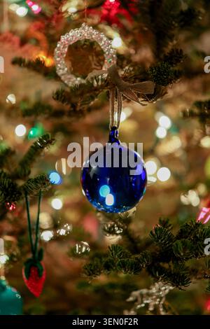 Blue glass ornament hanging on a decorated Christmas tree with colorful lights. Stock Photo