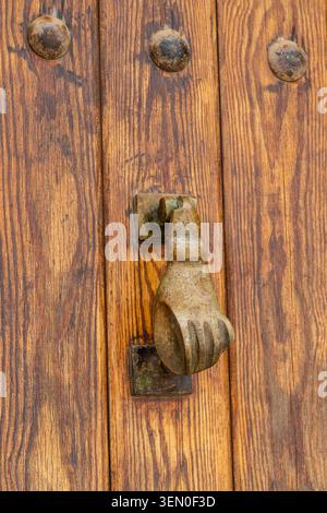 Rustic wooden door with a vintage metal hand-shaped knocker in focus. Stock Photo