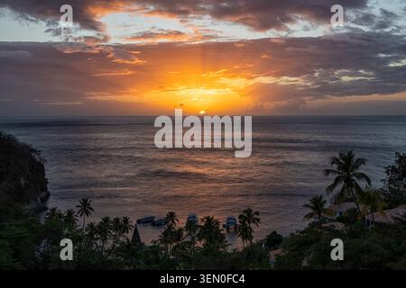 Sunset over a tranquil ocean with silhouetted palm trees and boats in the foreground. Stock Photo