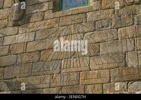 Ancient stone wall with a carved sundial and Roman numerals in sunlight. Stock Photo
