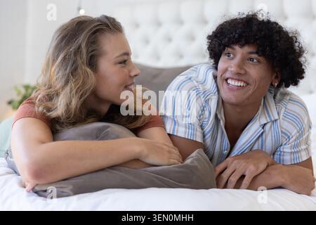 Couple lying on bed facing each other, woman propping on gray pillow, man smiling Stock Photo