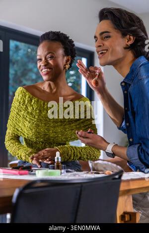 Female client in green top smiling, male makeup artist demonstrating foundation on wooden table Stock Photo