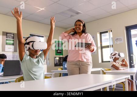 African American teacher holding tablet leading children in VR lesson in class using VR gear Stock Photo