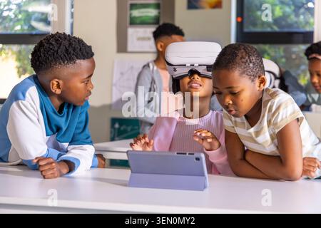 African American children trying VR using white headset and tablet in folio at classroom table Stock Photo