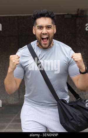 African American man in grey sportswear cheering, clenching fists under overhang with duffel strap Stock Photo