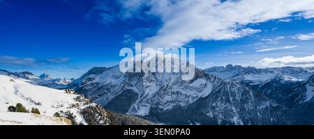 Snow-covered mountain range under a bright blue sky with scattered clouds. Stock Photo