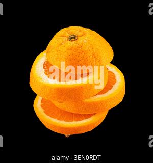 Whole orange with stacked slices showing juicy flesh, isolated on black background with visible juice droplets. Stock Photo
