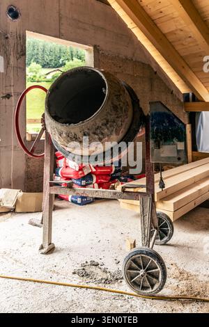 A concrete mixer stands prominently within an unfinished building under construction. The mixer, with its rotating drum and sturdy wheels, is surround Stock Photo