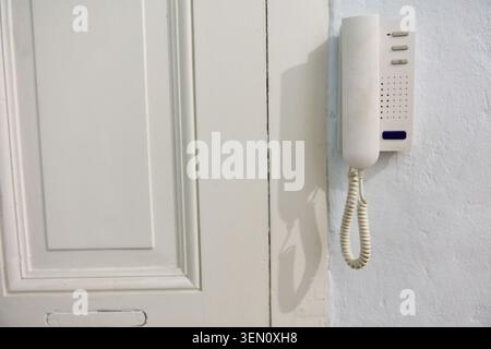 An old apartment intercom system is mounted on a white wall next to a classic white door in a building in Berlin Prenzlauer Berg, showcasing the pre r Stock Photo