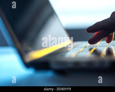 Fingers touch glowing keyboard of a laptop in a dimly lit room. Stock Photo