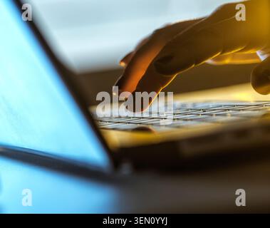 Hand typing on a laptop keyboard in a dimly lit setting with blue and yellow hues. Stock Photo