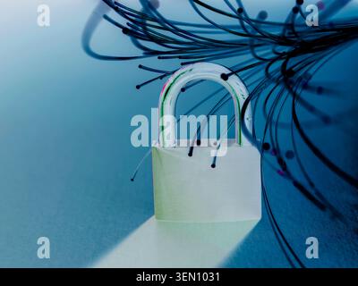 A padlock entangled with fiber optic cables on a reflective blue surface. Stock Photo