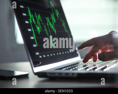 Hand typing on a laptop keyboard with stock market graph on screen Stock Photo