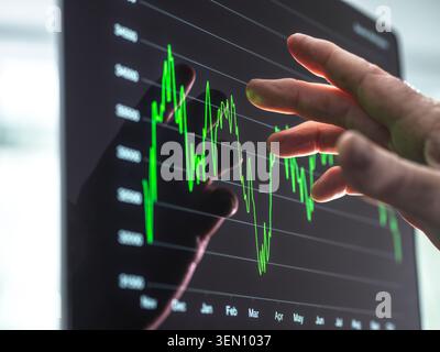 Hand touching digital graph on a screen showing fluctuating financial data. Stock Photo