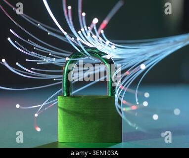 Green padlock surrounded by glowing fiber optic cables on a reflective surface. Stock Photo