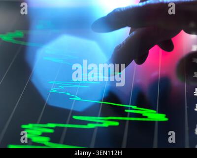 A hand interacts with a tablet displaying a glowing financial chart in blue and green hues. Stock Photo