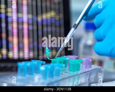 Gloved hand using pipette with colorful test tubes in a lab setting with data screen behind. Stock Photo