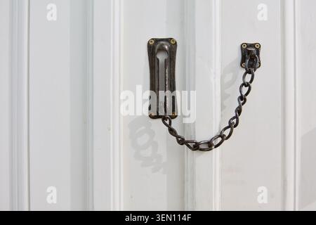 A home security door chain lock is prominently featured on a white wooden door, emphasizing safety and protection for residential properties. This clo Stock Photo