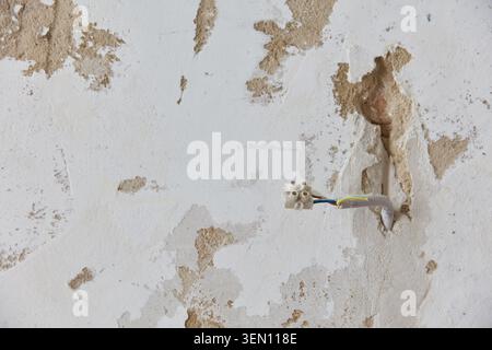 This captures a renovation project in an old Berlin apartment, showcasing exposed electrical wires on a damaged wall. It is illustrating construction, Stock Photo
