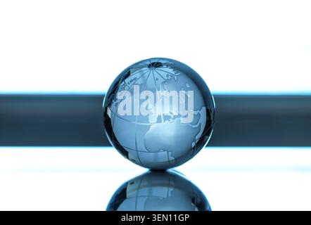 Transparent glass globe with etched continents on reflective surface. Stock Photo