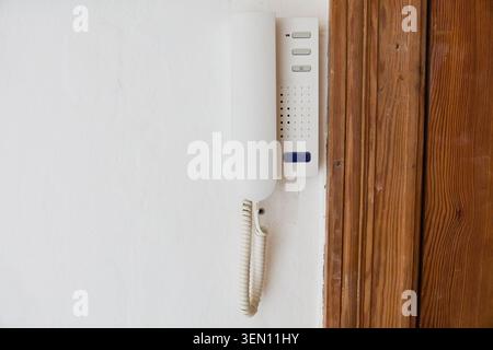 Vintage intercom system mounted on a white wall next to a wooden door frame in an old Berlin apartment building, highlighting the need for renovation Stock Photo