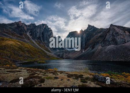 Stunning mountain range with a lake and sun peeking through dramatic clouds. Stock Photo
