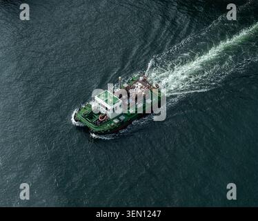 High Angle Aerial View of a Small Green Industrial Work Boat Cruising on Deep Blue Water Stock Photo