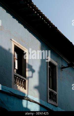 Two windows with wrought iron railings on a blue stucco building facade under sunlight. Stock Photo