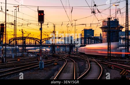 Fast trains leaving and arriving at Munich main station (Germany) in warm evening light. Blurred light traces. Railway infrastructure, signals, gliste Stock Photo