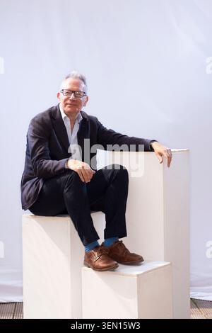 Fintan O'Toole stands next to a rubber duck painted in the colors of the British flag. He leans on a white pedestal. Stock Photo