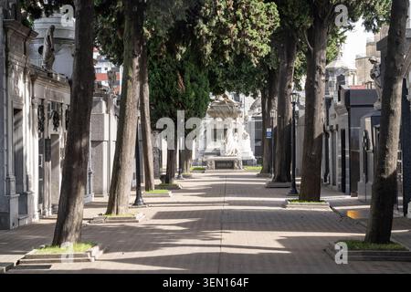 A dramatic perspective view inside La Recoleta Cemetery in Buenos Aires, Argentina. The central stone pathway is lined with historic mausoleums and ta Stock Photo