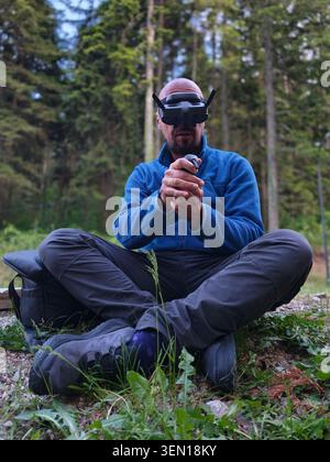Man Wearing FPV Drone Goggles Using Remote Controller While Sitting in Forest Outdoors Stock Photo