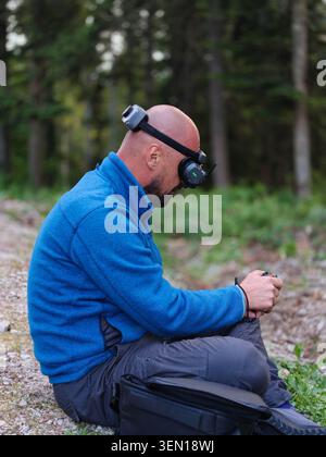 Man Wearing FPV Drone Goggles Sitting Outdoors Controlling Remote Controller in Forest Stock Photo