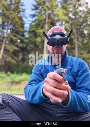 FPV Drone Pilot Wearing Goggles and Holding Controller While Flying Quadcopter in Forest Outdoors Stock Photo