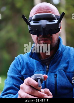 Bald Man Wearing FPV Drone Goggles Piloting Remote Controller Outdoors With Focused Expression Stock Photo
