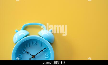Cropped view of a blue retro alarm clock in the bottom left corner on a yellow background, ideal for text placement. Stock Photo