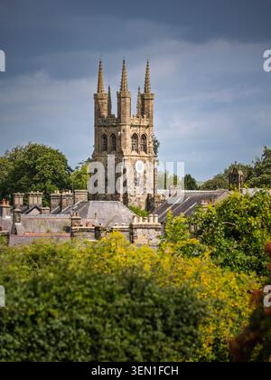 Low angle view looking through dense green garden trees and shrubbery towards the rising stone tower of St John the Baptist Church in Tideswell villag Stock Photo