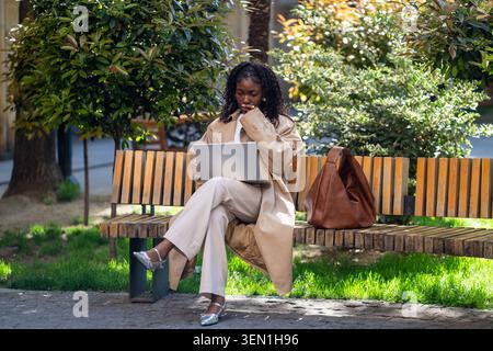 Thoughtful african american woman student working on laptop outside after lessons in university. Stock Photo