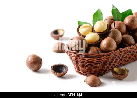 Premium macadamia nuts displayed in a woven wicker basket with cracked shells revealing creamy kernels, complemented by fresh green leaves. Arranged o Stock Photo