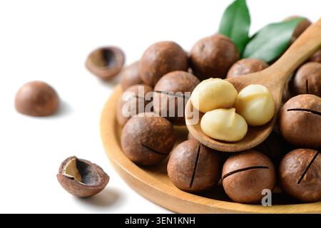 Close-up of fresh macadamia kernels on a wooden spoon surrounded by macadamia nuts in shells on a wooden plate with green leaves. Healthy premium food Stock Photo
