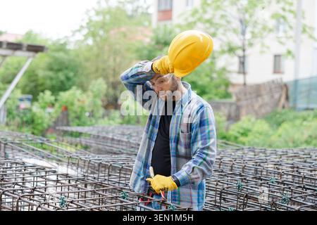 Construction worker wiping sweat from his forehead, taking a break from hard physical labor while building a rebar cage Stock Photo