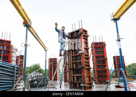 Construction worker in hard hat and safety glasses climbing ladder, setting metal formwork for a reinforced concrete column Stock Photo