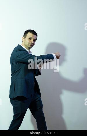 Vikram Paralkar stands in a formal outfit with a serious look as he makes a fist. His shadow is visible on the plain wall behind him. The setting appe Stock Photo
