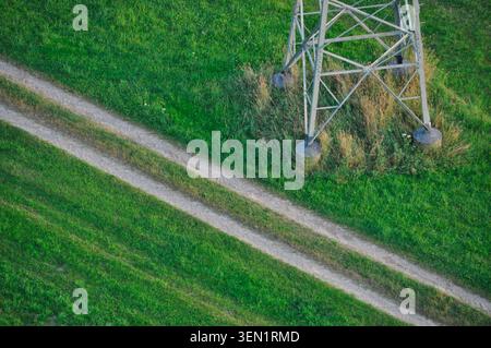 Aerial view of straight field path in green meadow next to foot of high-voltage pylon Stock Photo