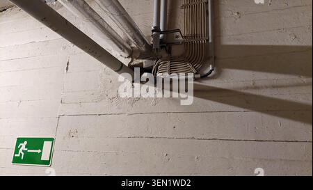 Insulated pipework and surface-mounted electrical installation on white wall and ceiling with shading Stock Photo